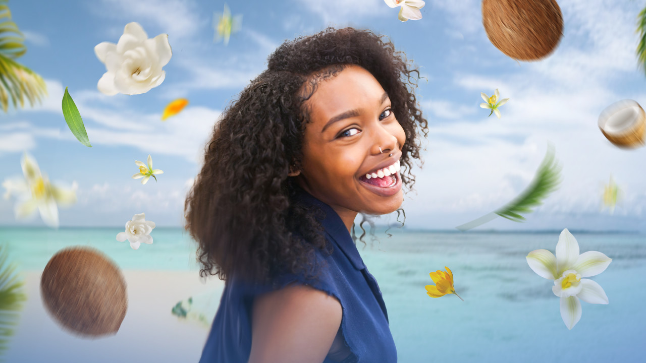 Woman smiling on a beach surrounded by flowers and coconuts